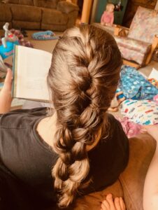The mess of motherhood surrounds Amy as her daughter braids her hair.